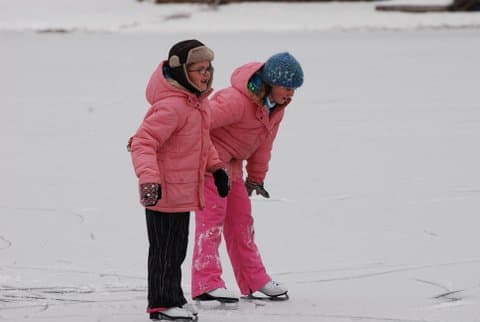 Two children in winter clothing joyfully skate on an ice surface.