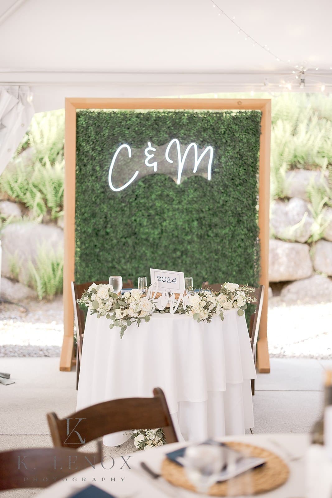 A beautifully decorated table with a floral arrangement and a neon sign reading "C & M" in front of a greenery backdrop.