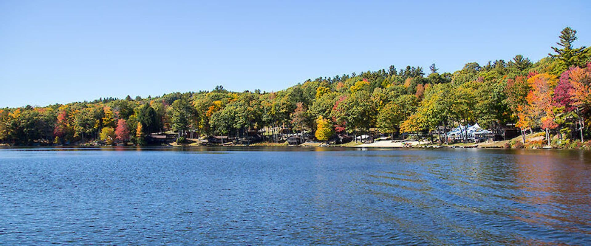 A serene lake surrounded by vibrant autumn trees under a clear blue sky.