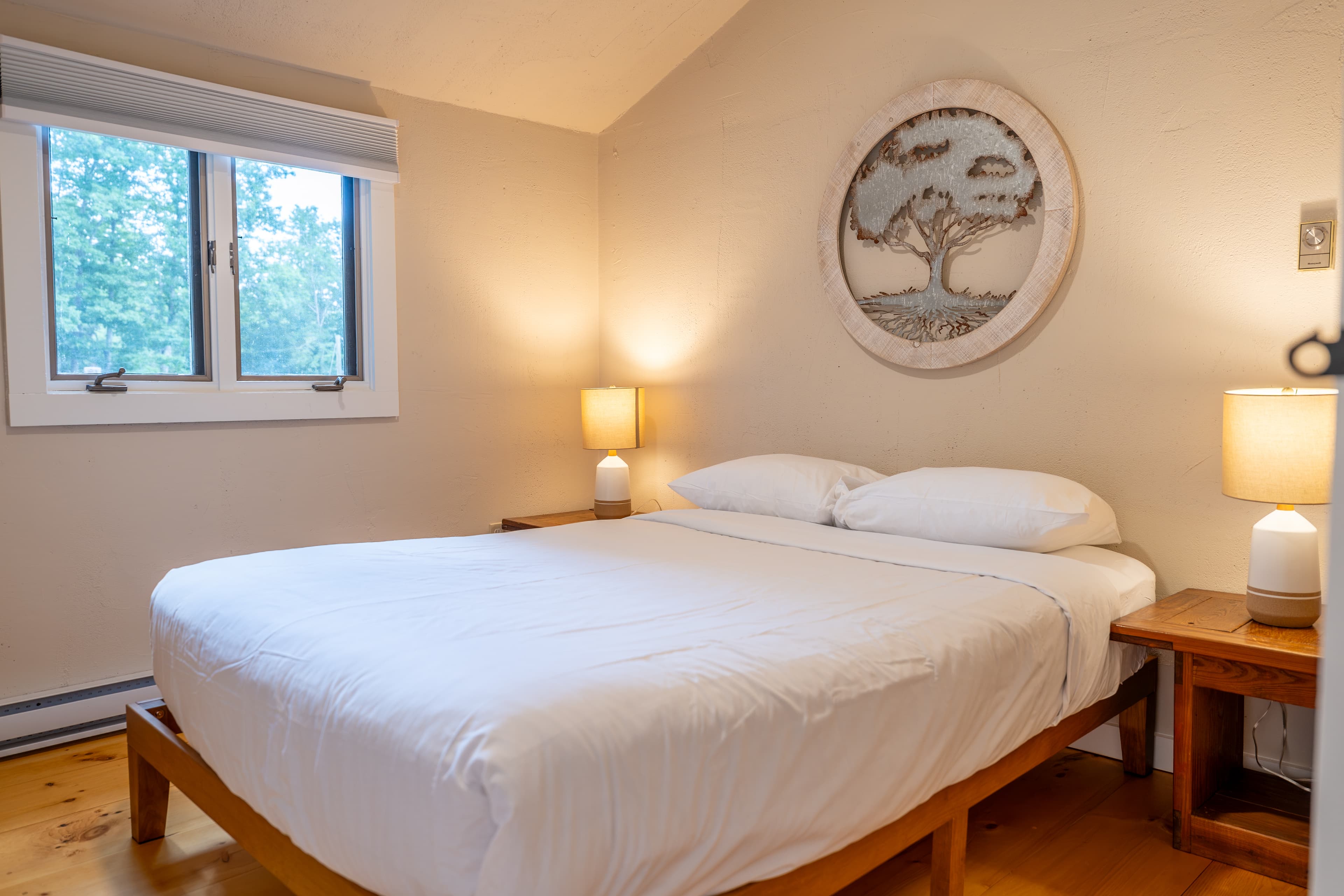 A cozy cabin bedroom with a vaulted ceiling, a bed with a geometric quilt, a bedside lamp, and a curtained window.
